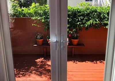 White French doors, recently installed with expert craftsmanship, open to a sunlit patio adorned with potted plants and lush greenery.