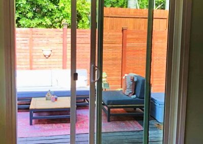 The glass sliding door installation opens to a patio with outdoor seating, a table, rug, and a wooden privacy fence.