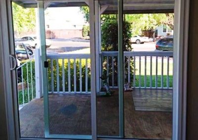 Sliding glass doors, expertly installed, open to a porch with a white railing and a view of a suburban street in the daytime.