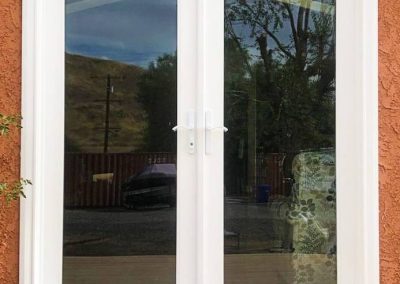 White-framed glass double doors, expertly installed, reflect an outdoor scene with a tree and fence.