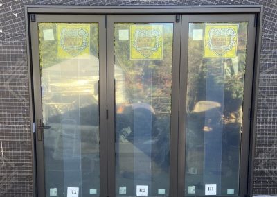 Three-panel glass sliding door with a reflective surface, elegantly framed in black, undergoing door installation.