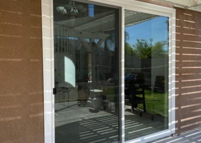 The newly completed door installation features sliding glass that beautifully reflects a backyard patio, with a pergola casting elegant striped shadows.