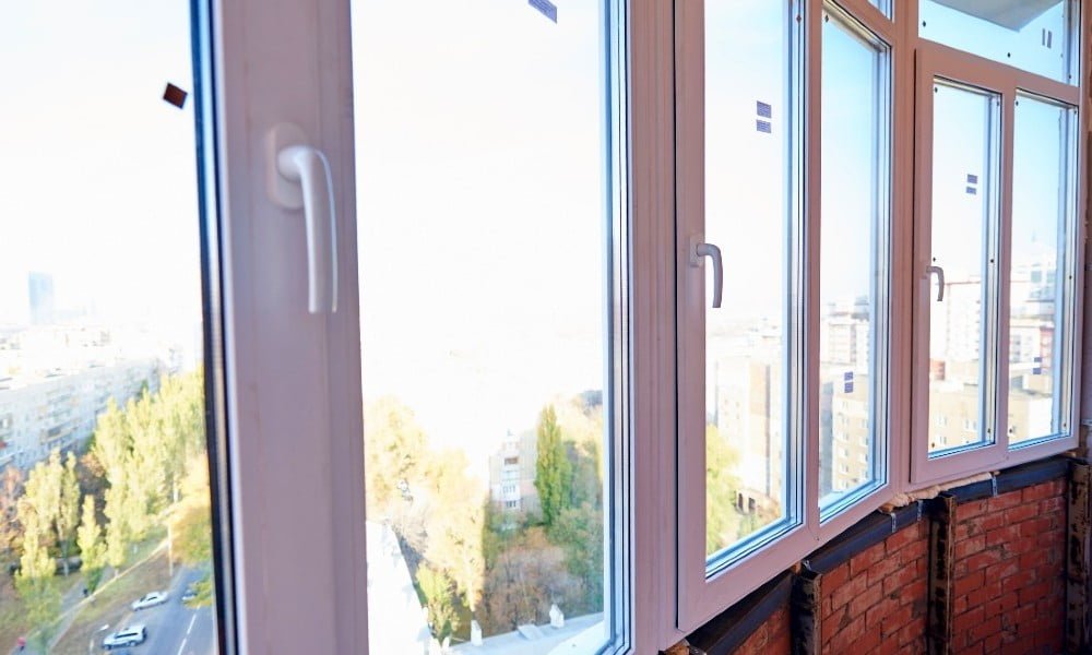 A row of large glass windows with white frames, expertly installed, overlooks a cityscape adorned with trees and buildings.