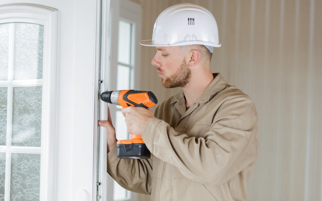 Man in a hard hat using a power drill to install or fix a door indoors.