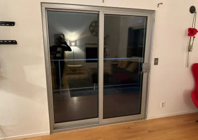 Sliding glass door with reflections, showing a living room with a couch, wall art, and a red chair.