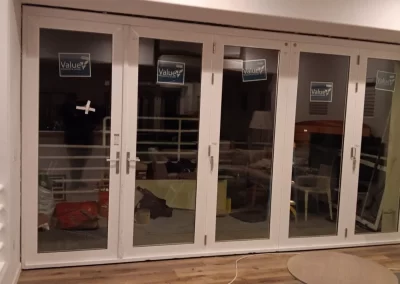 Large white-framed glass doors with Value stickers, leading to a room with furniture and various items inside.