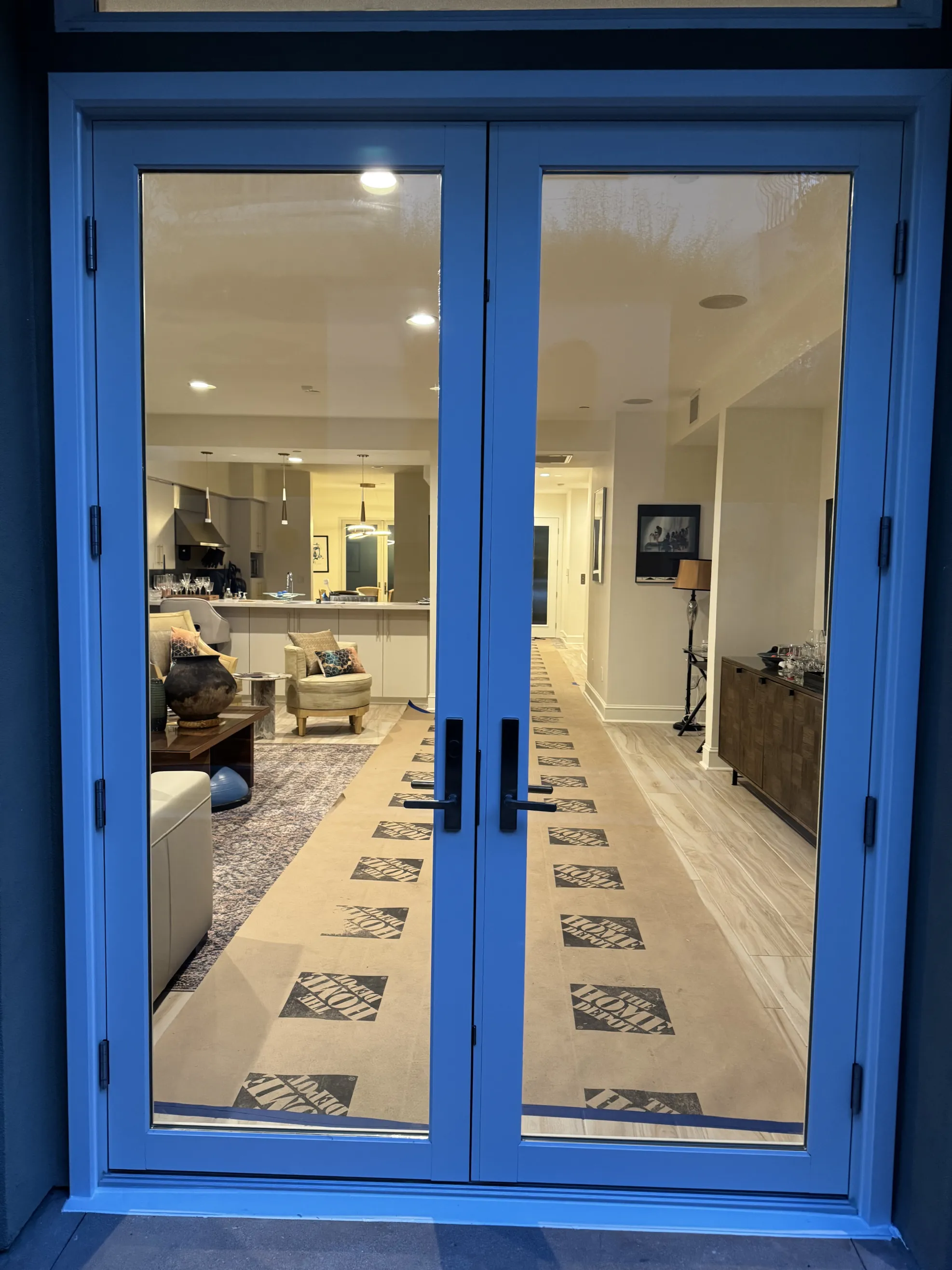 Double glass doors with black handles open to a modern, well-lit kitchen and living room interior.