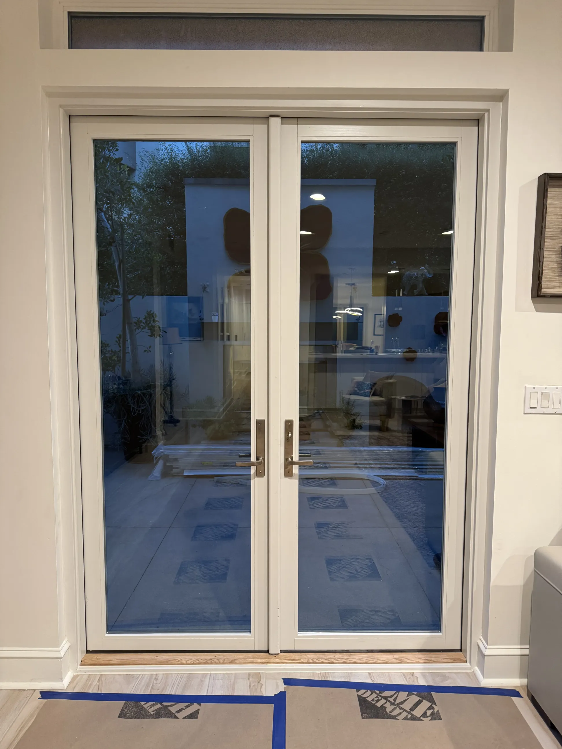 Glass double doors with white frames, showing a patio area and trees outside at dusk.